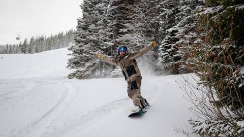snowboarder excitedly riding through snow near trees at Schweitzer