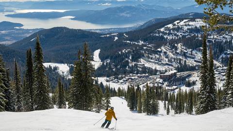 skier skiing down slope with lake pend oreille and Schweitzer village in the background