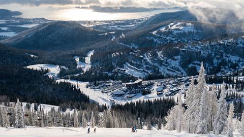 image of skier from a distance stopped on the slopes with view of lake pend oreille and village in the background