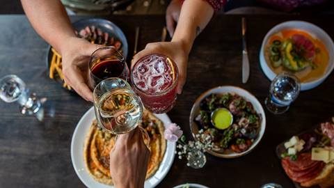people doing cheers with their glasses above table full of food
