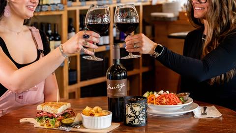 two people holding up their wine glasses to cheers with plates of food in front of them