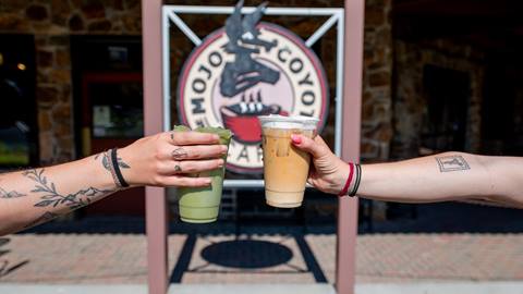 image of two people holding out their drinks from mojo in front of the sign