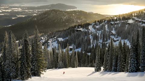 image of solo skier riding down trail with lake pend oreille in the background
