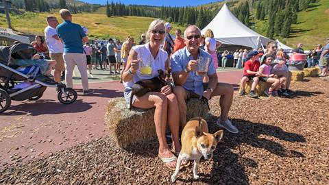 Couple with their dog lifting their mugs of beer and smiling at Schweitzer's Fall Fest