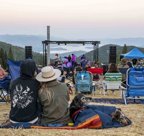 a couple and their dogs relax on a blanket while watching outdoor live music during summer activities at schweitzer