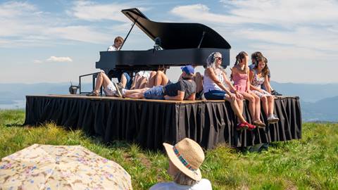 people sitting on platform with grand piano as they listen to live performance at Schweitzer