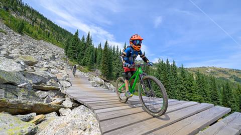 child biking on green mountain bike at Schweitzer going down wood plank trail