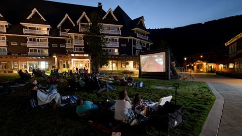 Group of people sitting on lawn and watching movie on inflatable screen