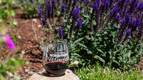 Northwest Winefest 2025 glassware with red wine in glass surrounded by beautiful flowers at Schweitzer