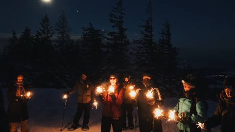 people holding sparklers while on moonlight snowshoe hike