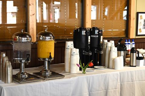 A banquet table at Schweitzer is set with dispensers for water and juice alongside coffee carafes and stacks of cups for a catered event