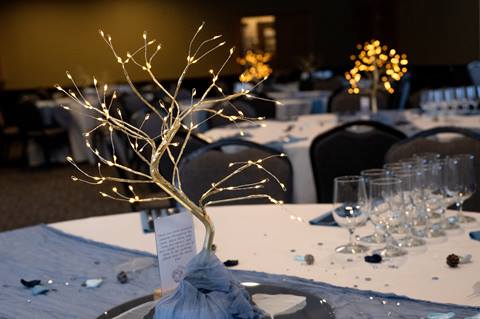 An elegant, gold-branched tree centerpiece with warm LED lights sits on a white linen table during a formal banquet at Schweitzer.