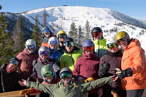 group of people smiling on the rowdy grouse deck with the slopes at Schweitzer in the background
