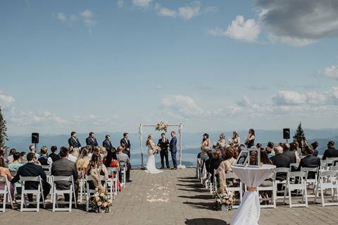 Guests sit in white chairs for an outdoor wedding ceremony at Schweitzer, overlooking a scenic mountain landscape and Lake Pend Oreille.