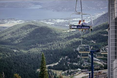 Newly married couple riding a chairlift with a Just Married sign at Schweitzer Mountain Resort overlooking Lake Pend Oreille and lush green valleys