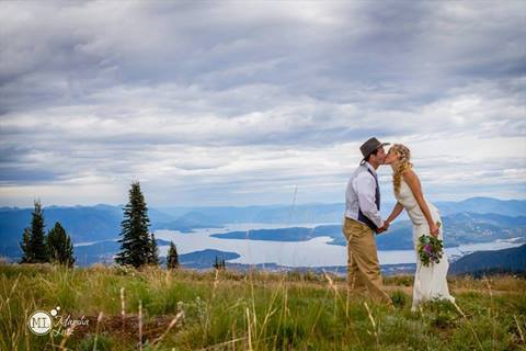 Bride and groom kissing on a grassy mountaintop overlooking Lake Pend Oreille and surrounding mountain ranges at Schweitzer Mountain Resort