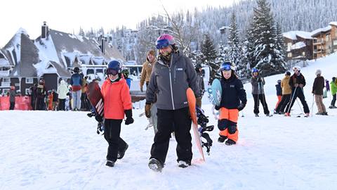 Snowboard instructor and group of kids with snowboards walking