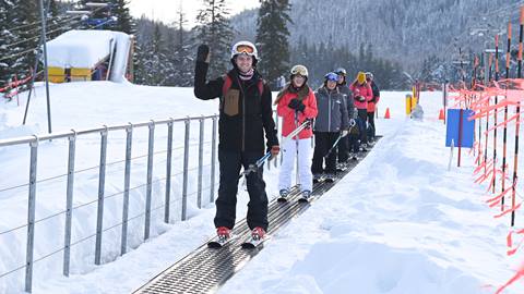 a group of smiling students rides the magic carpet during snowboarding & ski lessons from the schweitzer mountain resort ski school