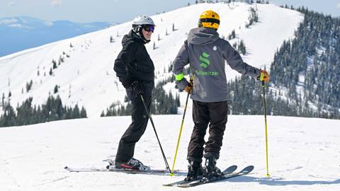 an instructor and a student stand on a mountain peak during a private ski lesson at schweitzer mountain resort