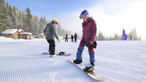 an instructor works one-on-one with a student on a groomed slope during private snowboard lessons at schweitzer mountain resort