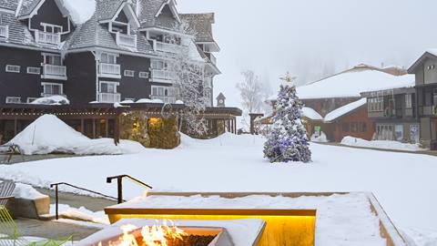 snowy courtyard outside selkirk lodge at schweitzer with a glowing fire pit and decorated winter tree