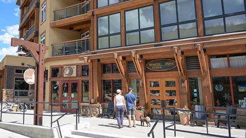Two people walking a dog in front of the White Pine Lodge entrance at Schweitzer