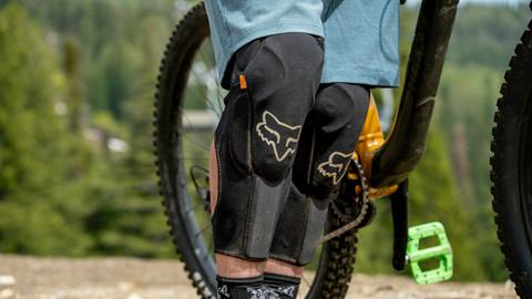 a man fits protective shin pads by his trail bike before riding at schweitzer