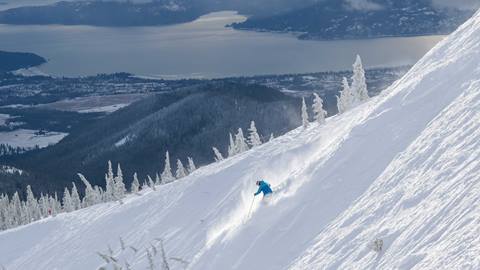 skier carving powder at Schweitzer with demo ski rentals with a winter lake view below
