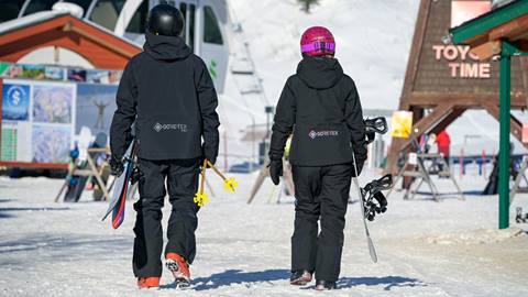 a skier and snowboarder wearing clothing rentals walking at schweitzer mountain in helmets and ski rentals