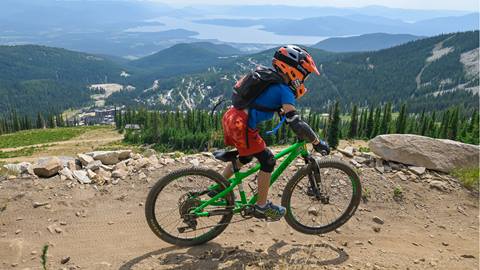 Young rider pedaling downhill on a green youth bike with helmet and pads at Schweitzer 