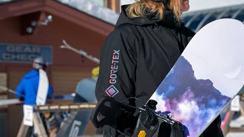 a person in a black gore-tex ski jacket rental holds a snowboard at schweitzer mountain