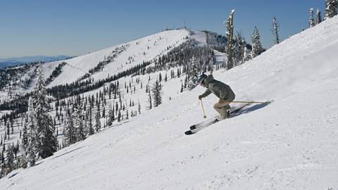 a skier making fresh turns at schweitzer using ski rentals with a view of lakeview triple in the background