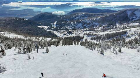 drone image of skiers going down groomed run with view of lake pend oreille in the background