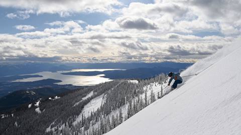skier going down steep run with view of lake pend oreille in the background