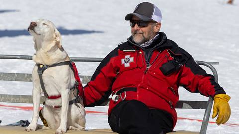 A ski patroller and an avalanche rescue dog sit together on a chairlift at Schweitzer.
