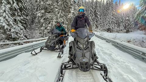 two men smiling on snowmobiles during schweitzer mountain snowmobile tours