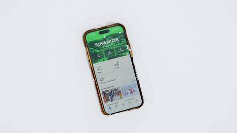 iphone in snow showing ikon pass app with schweitzer home page