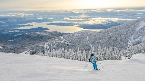 skier leisurely skiing down slopes with view of Lake Pend Oreille in the background