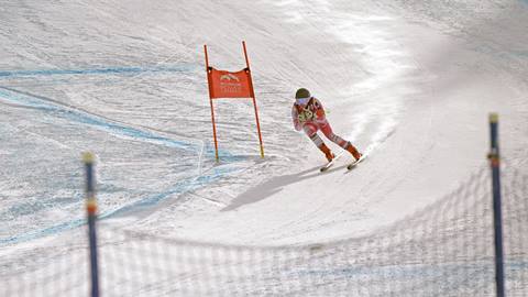 A ski racer in a tucked position speeds past an orange race gate on a groomed course at Schweitzer.