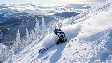 image of skier riding through powder with view of lake pend oreille in the background
