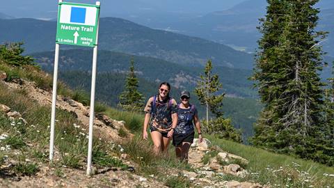 Two hikers enjoying a sunny climb along the Nature Trail at Schweitzer, a 2.5-mile route with panoramic views and well-marked hiking trails through alpine terrain
