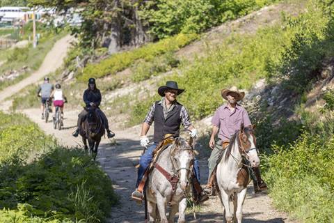 Horseback rides at Schweitzer Mountain with guests and guides traveling along a sunny forest trail surrounded by summer greenery