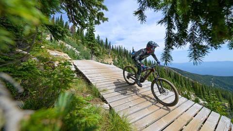 Rider leans into a bermed turn on Schweitzer's scenic mountain biking trails through evergreens