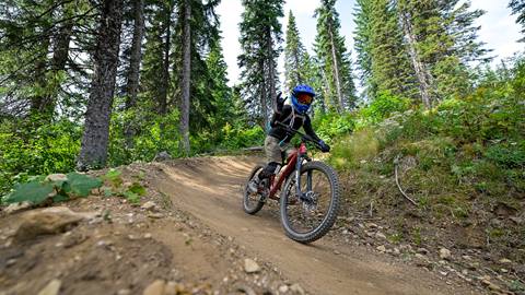a young cyclist throws up a rock on sign while trail riding at the youth summer bike camp at schweitzer
