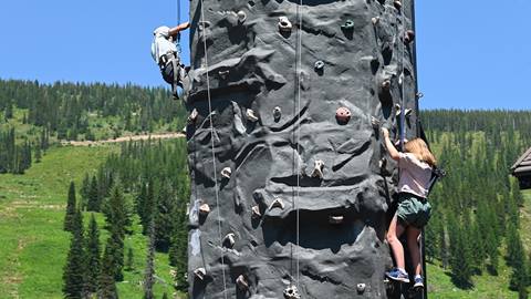 Two kids climbing the outdoor rock climbing wall at Schweitzer with forested mountains in the background