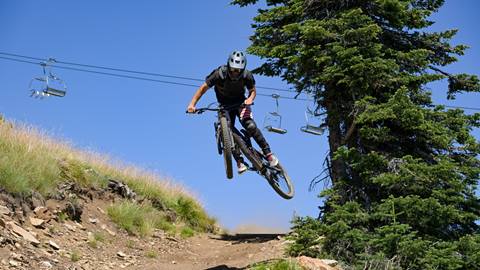 Mountain biker catches air off a jump beneath Schweitzer's chairlifts on an expert-level trail