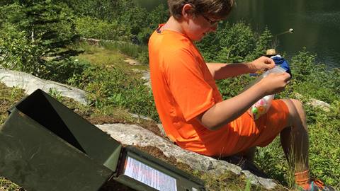 Child geocaching near a lake at Schweitzer, opening a hidden cache container and examining small treasures found during the outdoor adventure