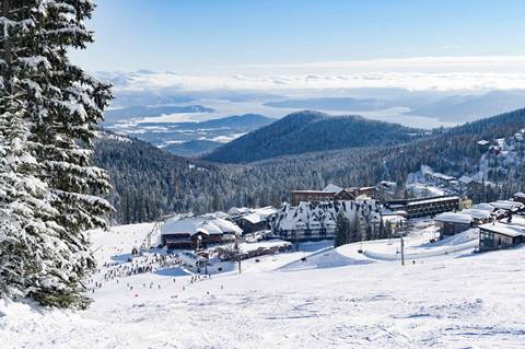 Panoramic view of Schweitzer Mountain Resort village covered in snow with Lake Pend Oreille and mountains in the background under a clear sky