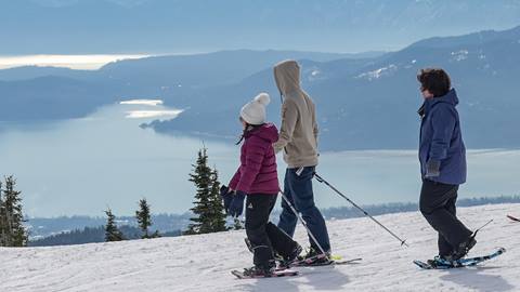 three people snowshoeing with lake pend oreille in the background