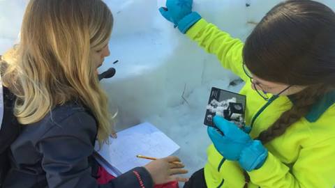 kids participating in a winter camp activity at schweitzer studying snow and taking notes during a hands-on learning session